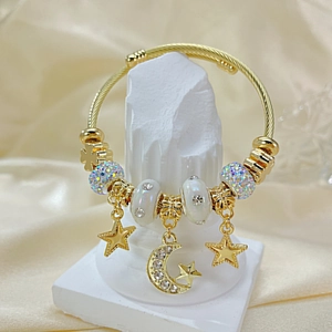 Close-up of gold wire bracelet with star and moon charms on a cream satin background