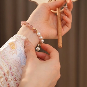 Elegant strawberry quartz and pearl beaded bracelet with gold accents on female wrist