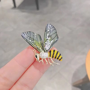 Detailed close-up of an enamel bee brooch with rhinestones and green wings on a finger