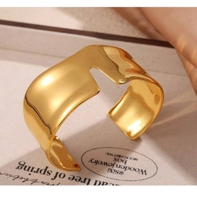 Close-up of golden irregular streamline open cuff bracelet with polished finish