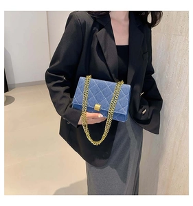 Close-up of blue denim square bag with quilted stitching and gold chain shoulder strap