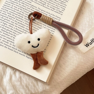 Close-up of a heart-shaped beige plush pendant with embroidery on an open book
