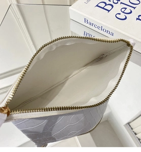 Macro view of white faux crocodile leather makeup bag with golden metal zipper detail