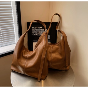 Detail view of two soft brown leather hobo bags against a minimalist background with blinds