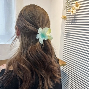 Rear view of a model wearing a large gradient blue-green plumeria flower hair claw clip