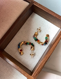 Macro view of gold C-shaped hoop earrings with colorful beaded wrap on fabric lining