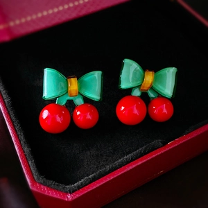 Détail de boucles d'oreilles cerises rouges avec nœuds verts dans un écrin de luxe