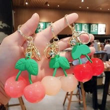 Primo piano di tre portachiavi a forma di ciliegia rosa e rossi con campanellini dorati