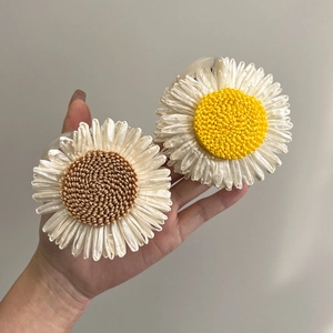 Pair of woven sunflower hair clips with daisy petals and braided centers held by hand