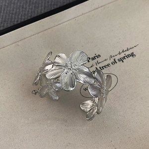Macro view of silver floral open cuff bracelet with brushed texture petals on cream card