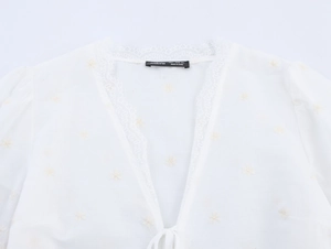 Gros plan du chemisier blanc à col en V avec bordure en dentelle et broderie florale