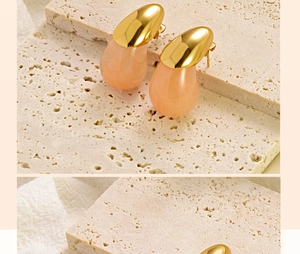 Detailed view of teardrop earrings with gold metal and pink resin on a stone surface