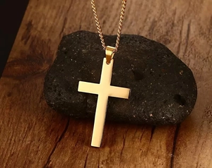 Detailed view of a gold cross necklace placed on a black volcanic rock with rustic wood base