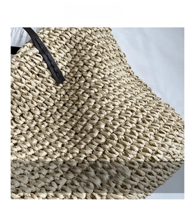Close-up of beige woven texture and brown leather handle stitching on the tote bag