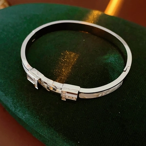 Detailed view of silver titanium steel T-shaped bangle with pavé zircons on green velvet