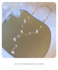 Detail view of a gold Y-shaped pearl necklace on a heart-shaped mirror with white feathers