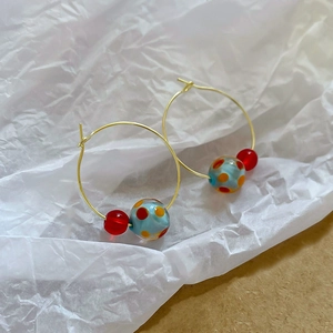 Detailed view of gold hoop earrings with blue orange-dotted and red resin beads on paper