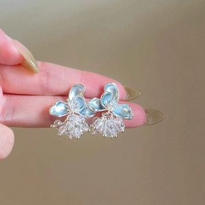 Close-up of elegant light blue flower earrings with crystal clusters held by hand