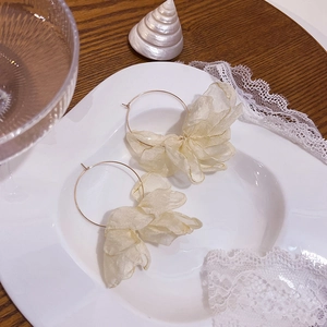 Dettaglio di orecchini a cerchio con fiori in tessuto crema su un piatto di porcellana bianca