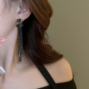 Detailed view of long black tassel earrings with sparkling rhinestones on model