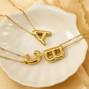 3D balloon initial necklaces in gold stainless steel displayed on a white shell plate