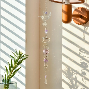 Detail of crystal suncatcher with metal hummingbird and purple beads casting rainbow light