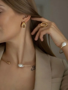 Detailed view of golden drop earrings and baroque pearl necklace worn by a model