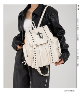 Detail of cream backpack featuring silver studs and gothic cross pendant on lychee texture
