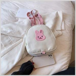 Flat lay of cream canvas kids backpack with pink straps and a cute cartoon rabbit patch