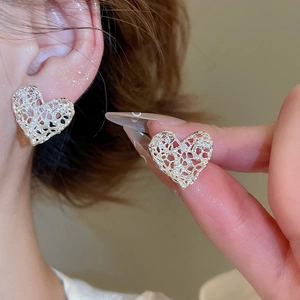 Detailed close-up of hollow heart-shaped silver earrings with intricate woven texture