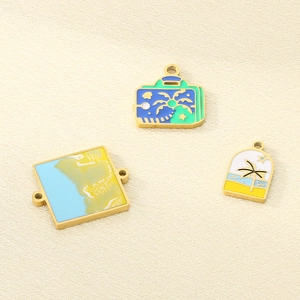 Close-up of beach-themed enamel charms featuring a suitcase, archway, and square pendant