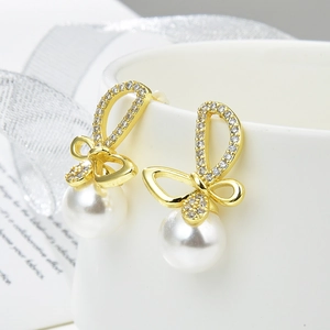 Detailed close-up of gold bow earrings with micro-pave zircons and hanging white pearls