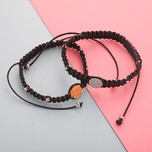Woven cord bracelets with gold and silver St. Benedict medals on a split pastel background