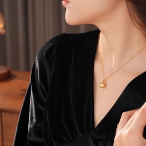 Close-up of 18k gold plated apple pendant necklace worn by a model on black velvet