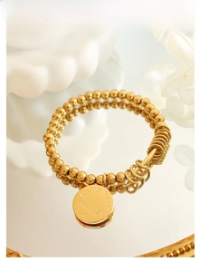 Macro shot of gold beaded bracelet featuring engraved round pendants and polished finish