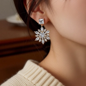 Close-up of 14k gold plated snowflake drop earrings with sparkling zircon on model ear