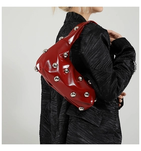 Detail of red patent leather shoulder bag with silver studs on black blazer outfit