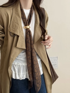Détail du foulard en soie cachemire marron foncé avec une boucle en métal doré sur modèle