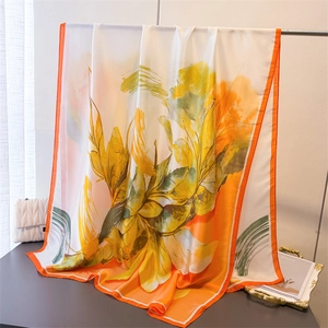 Detailed view of vibrant orange silk scarf with abstract green floral patterns and smooth texture