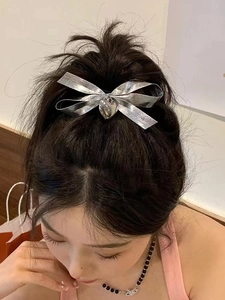 Detailed view of a silver metallic bow hair clip with heart pendant on a high ponytail