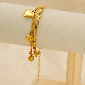 Détail d'un bracelet double couche doré avec cœur et perles sur un support à bijoux gris