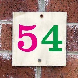 Détail du numéro 54 en vinyle étanche installé sur un mur de briques rouges avec vis