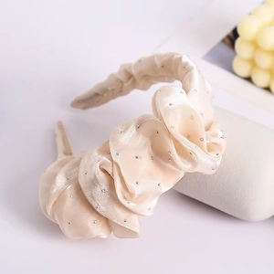 Detail of cream pleated headband with silver rhinestones on a soft silk fabric surface