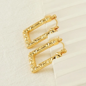 Detailed close-up of rectangular gold-plated earrings with unique hammered texture finish