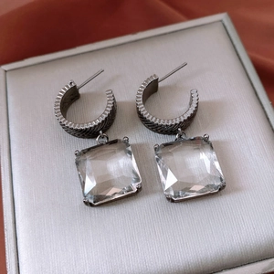 Close-up of C-shaped dark grey metal earrings with large square faceted glass crystals