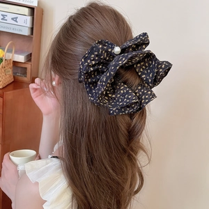 Detailed view of a large black bow hair claw with gold polka dots and a central white pearl