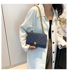 Detail of blue denim quilted square bag with gold chain strap and metal lock closure
