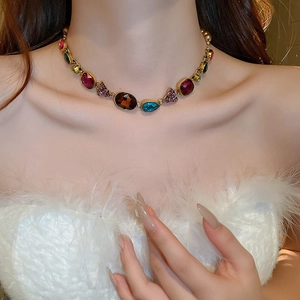 Close-up of vintage gold necklace with multi-color gemstones on elegant model outfit
