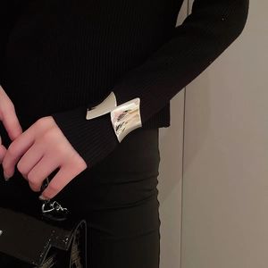 Dettaglio di un bracciale a polsino argento irregolare indossato sopra una manica nera