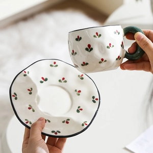 Close-up of hand-painted ceramic coffee cup and wavy saucer with red flower patterns